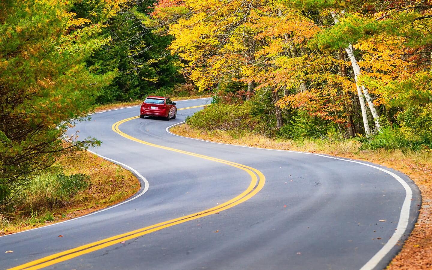 A red car driving on a curvy road. A red car driving on a curvy road.
