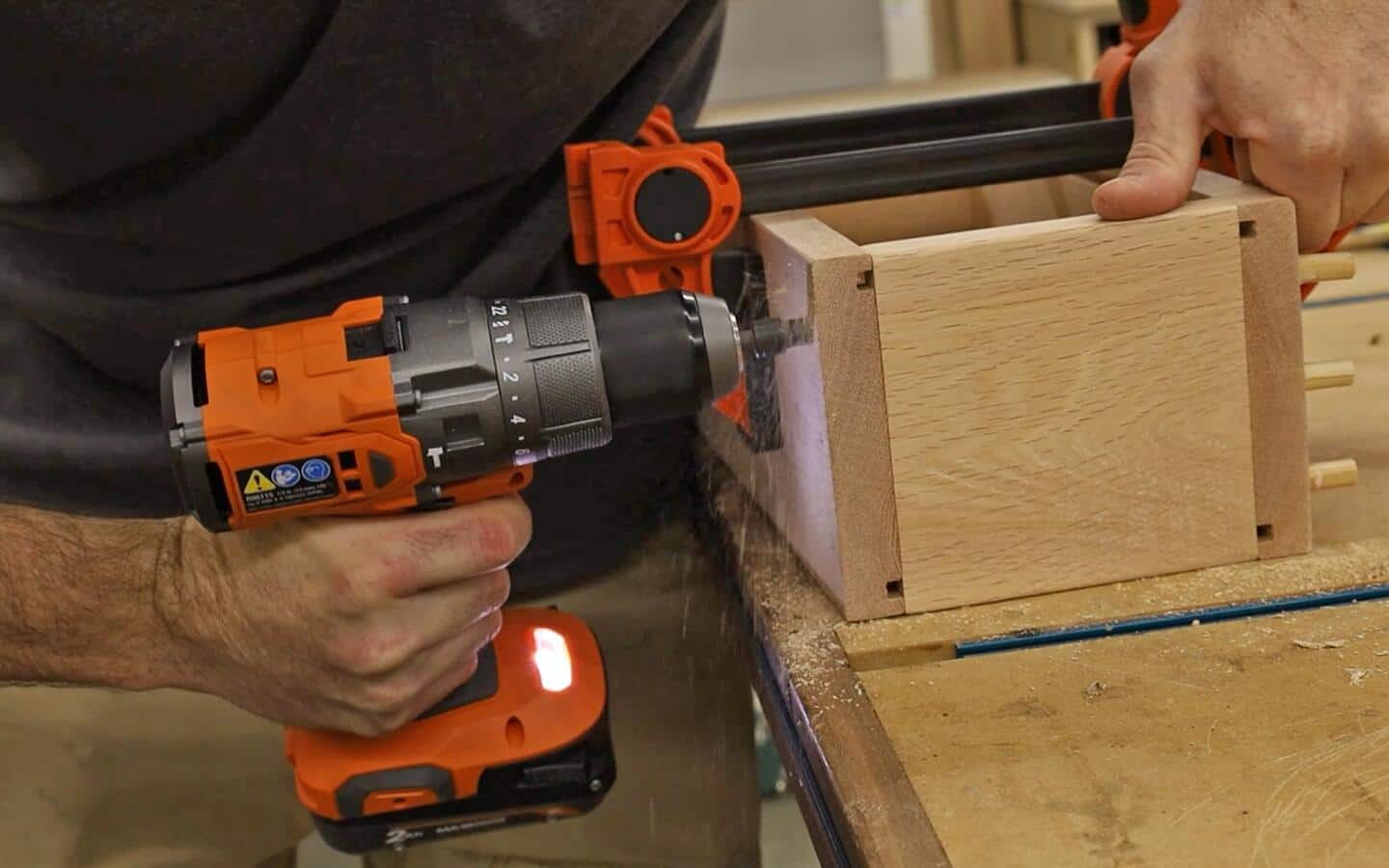 A person using a cordless drill to screw wood shelf and back boards together.