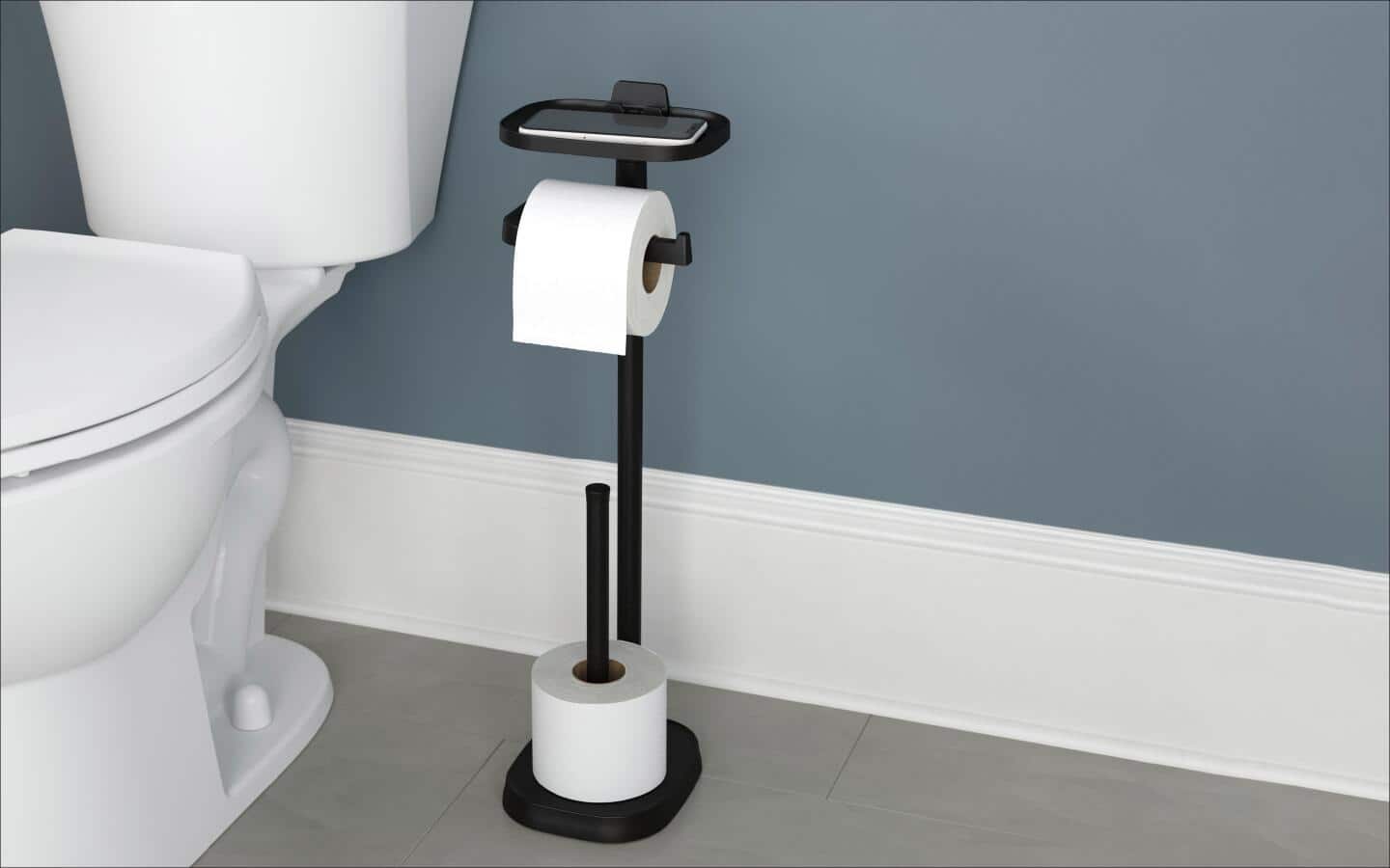 A freestanding toilet paper holder is located next to a toilet in a bathroom.