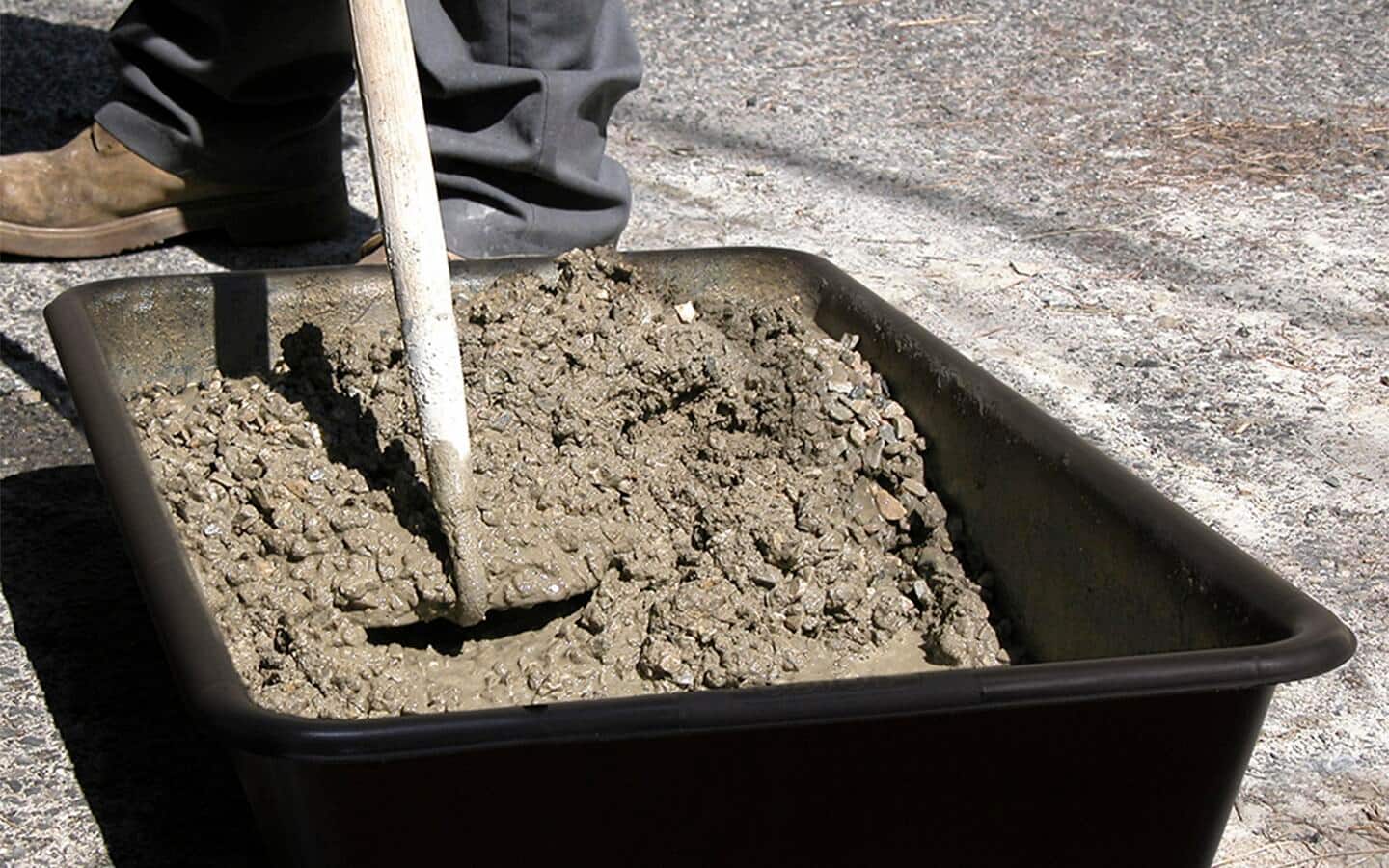 A person mixes wet concrete in a plastic container. A person mixes wet concrete in a plastic container.