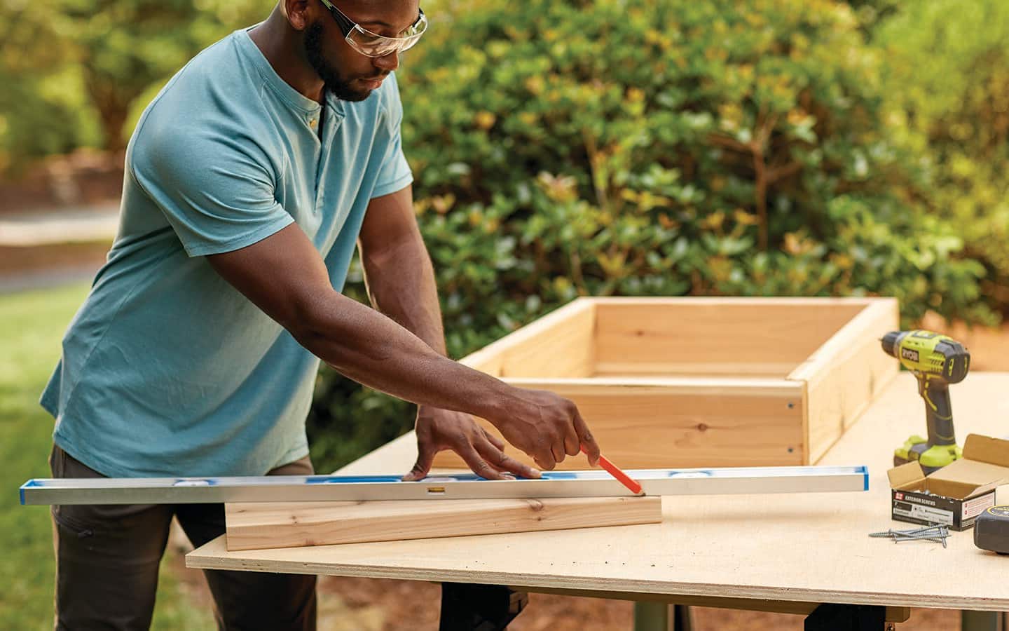 A man uses a straight edge and a pencil to draw a cut line on a board for a cold frame wedge.