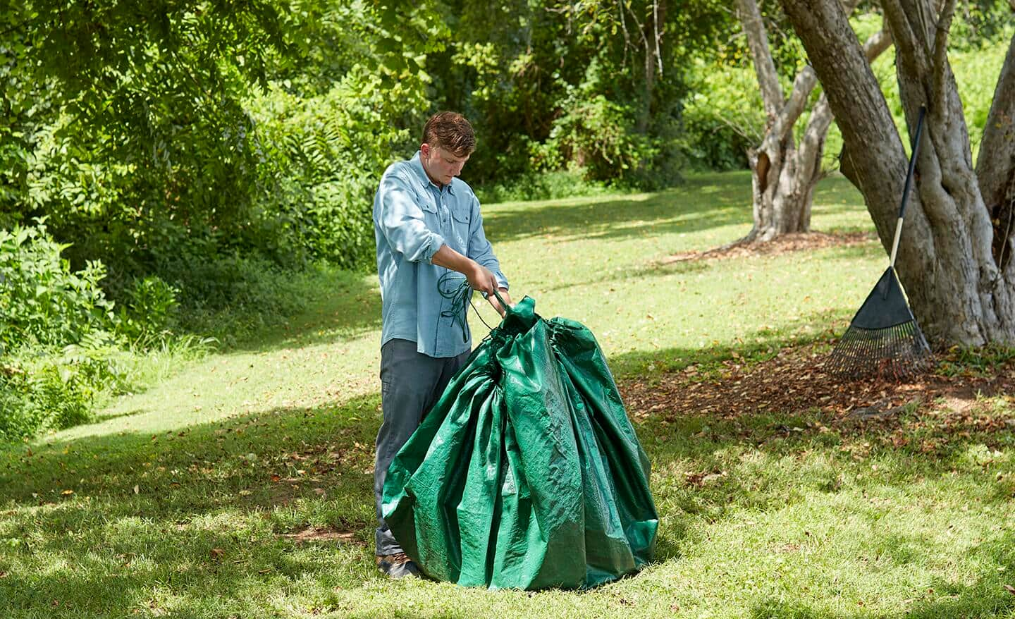 A person closes a green drawstring tarp outside.