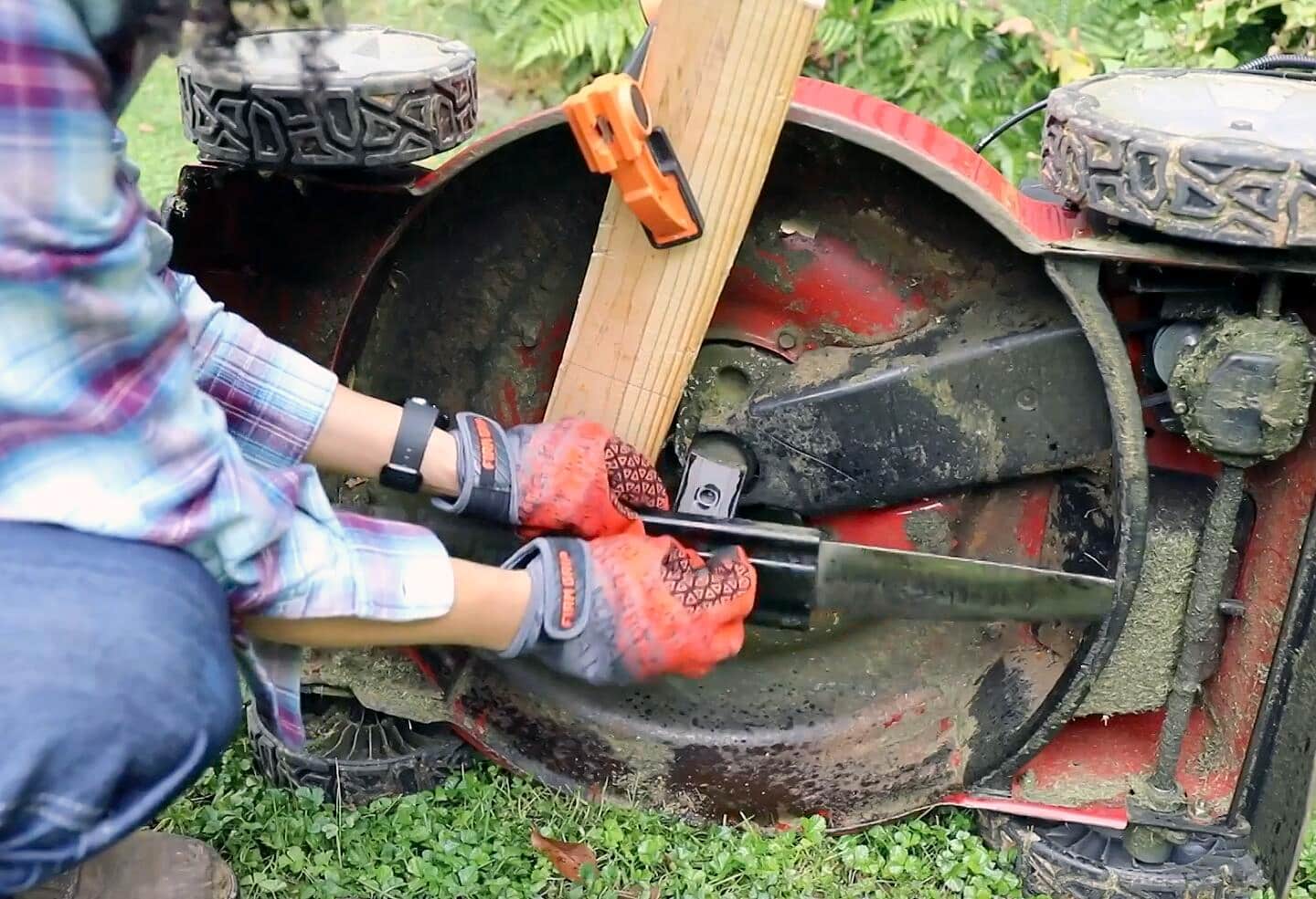 A person wearing gloves attaches a new blade to a lawn mower.