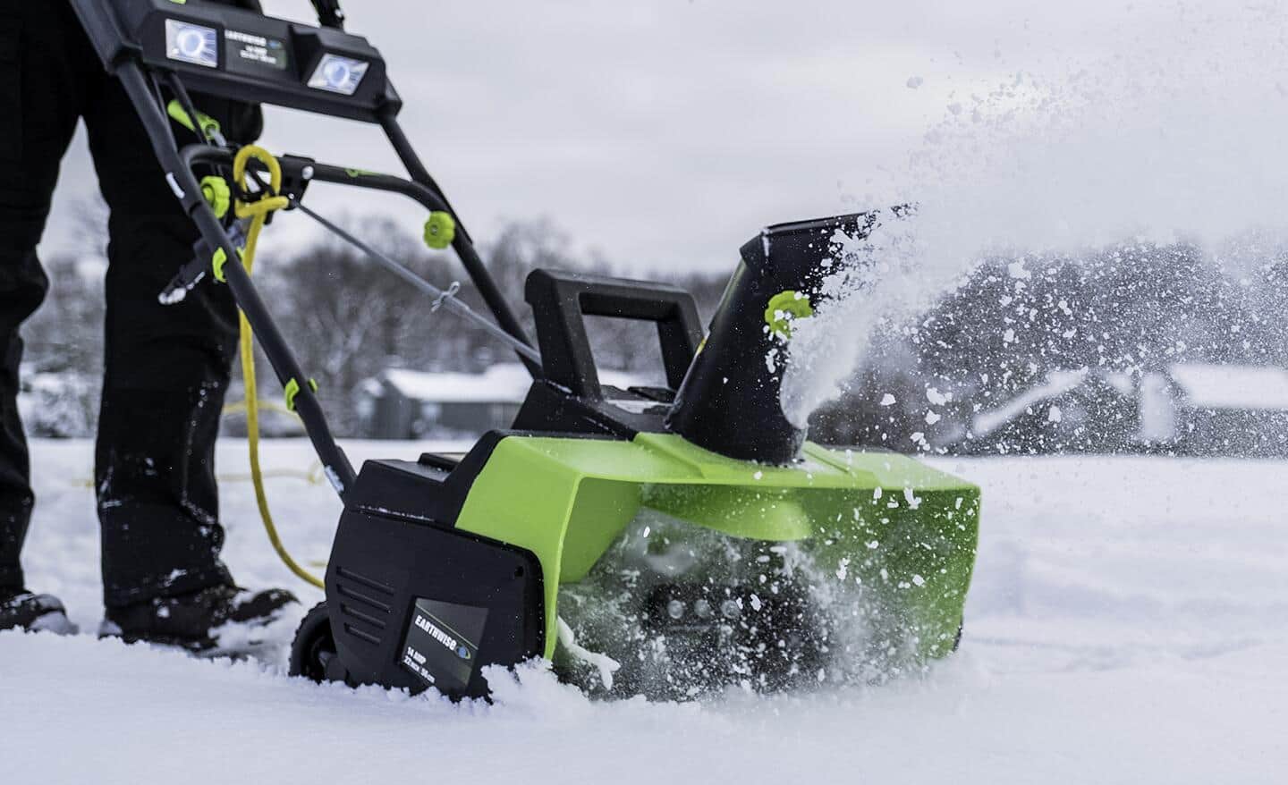 A person clearing snow with a green electric snow blower.