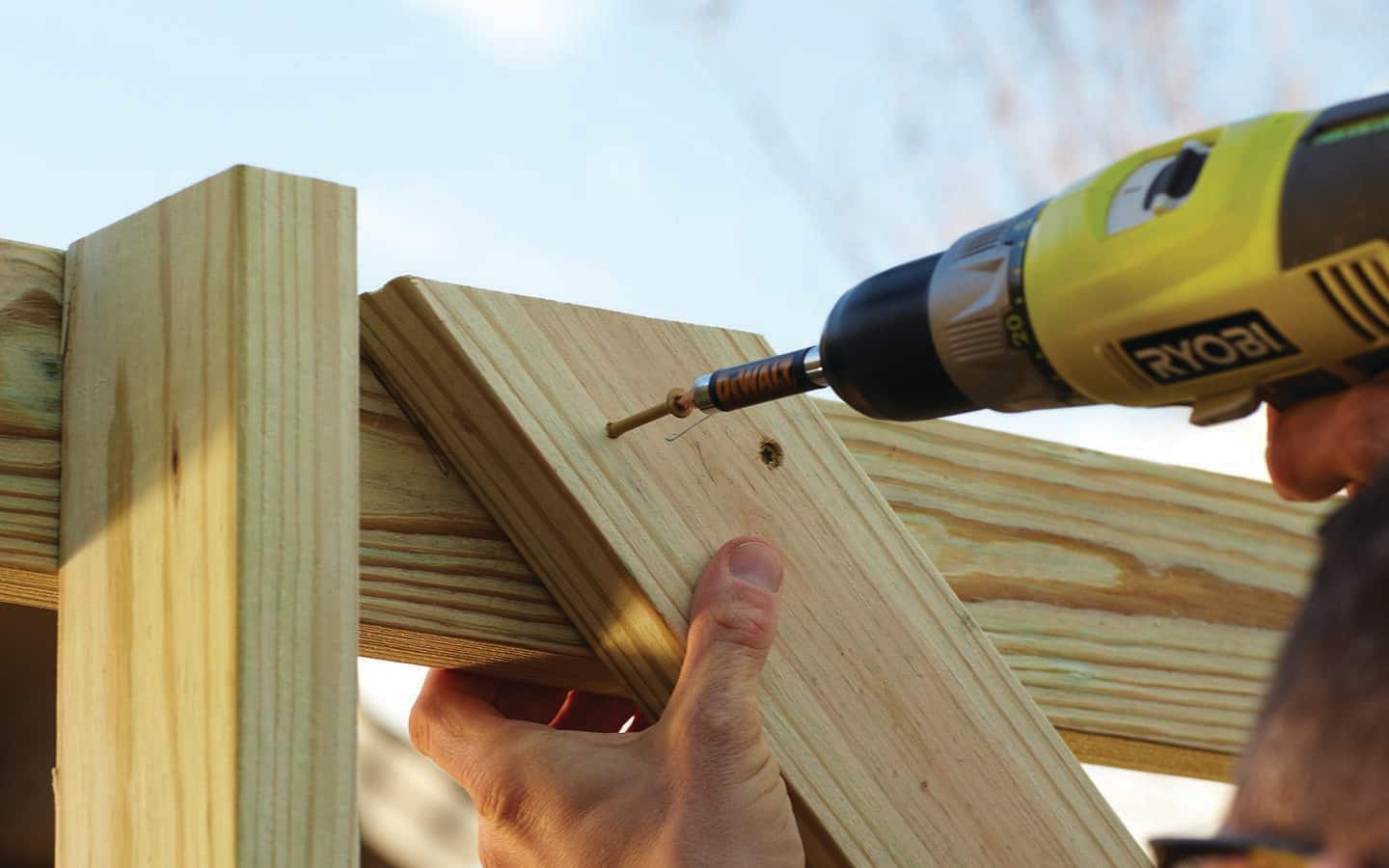 Someone uses a power drill to drive a cross brace into an enclosure's frame. Someone uses a power drill to drive a cross brace into an enclosure's frame.