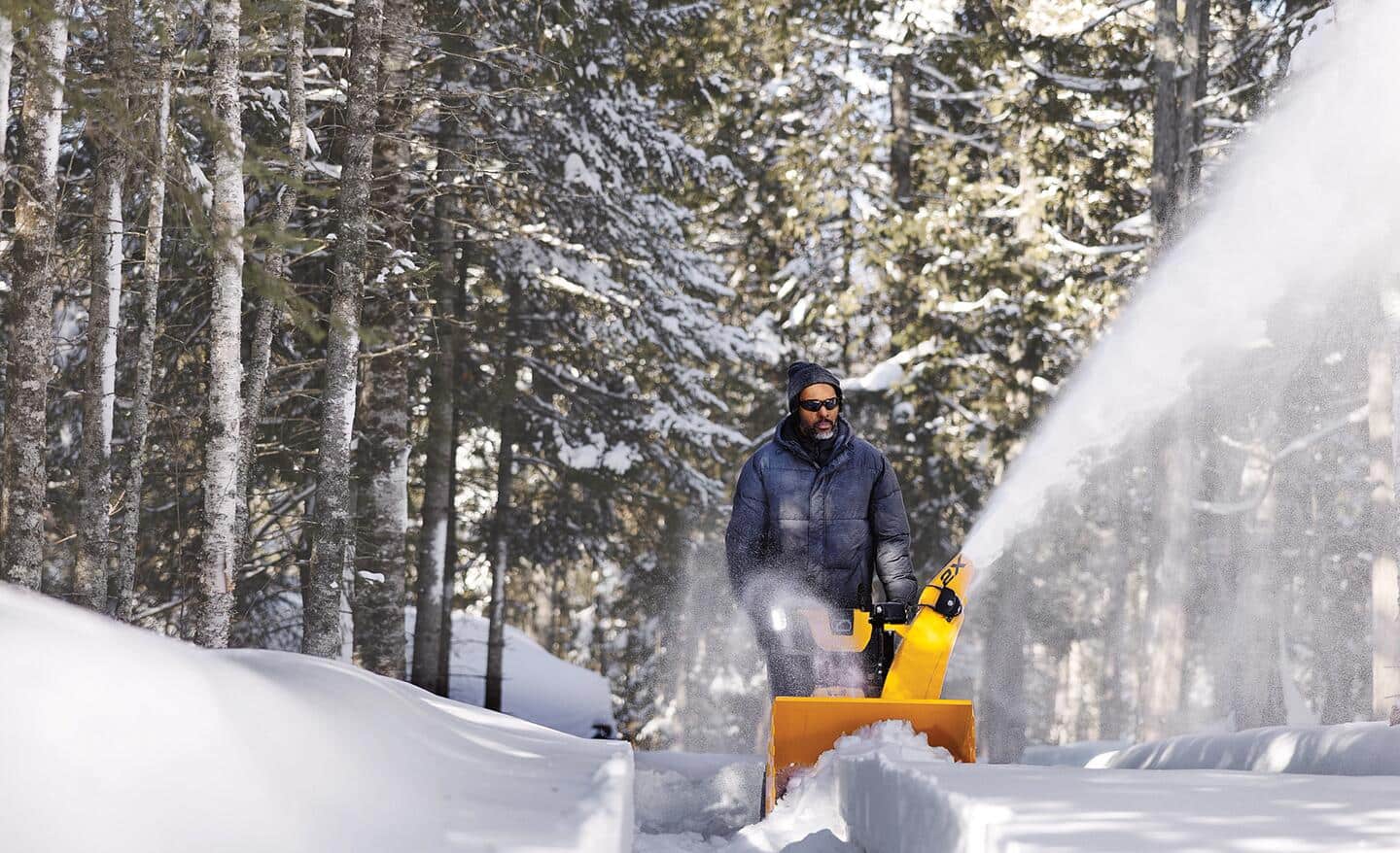 A person pushing a yellow snow blower to clear a path.
