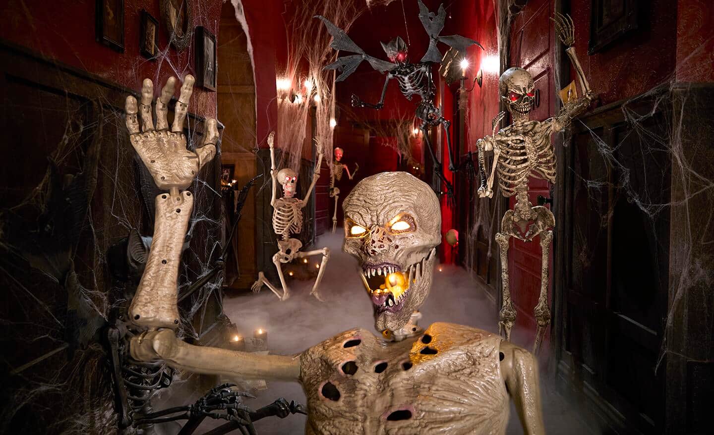 Skeletal creatures stand in a house decorated with fog and whispy webs. 