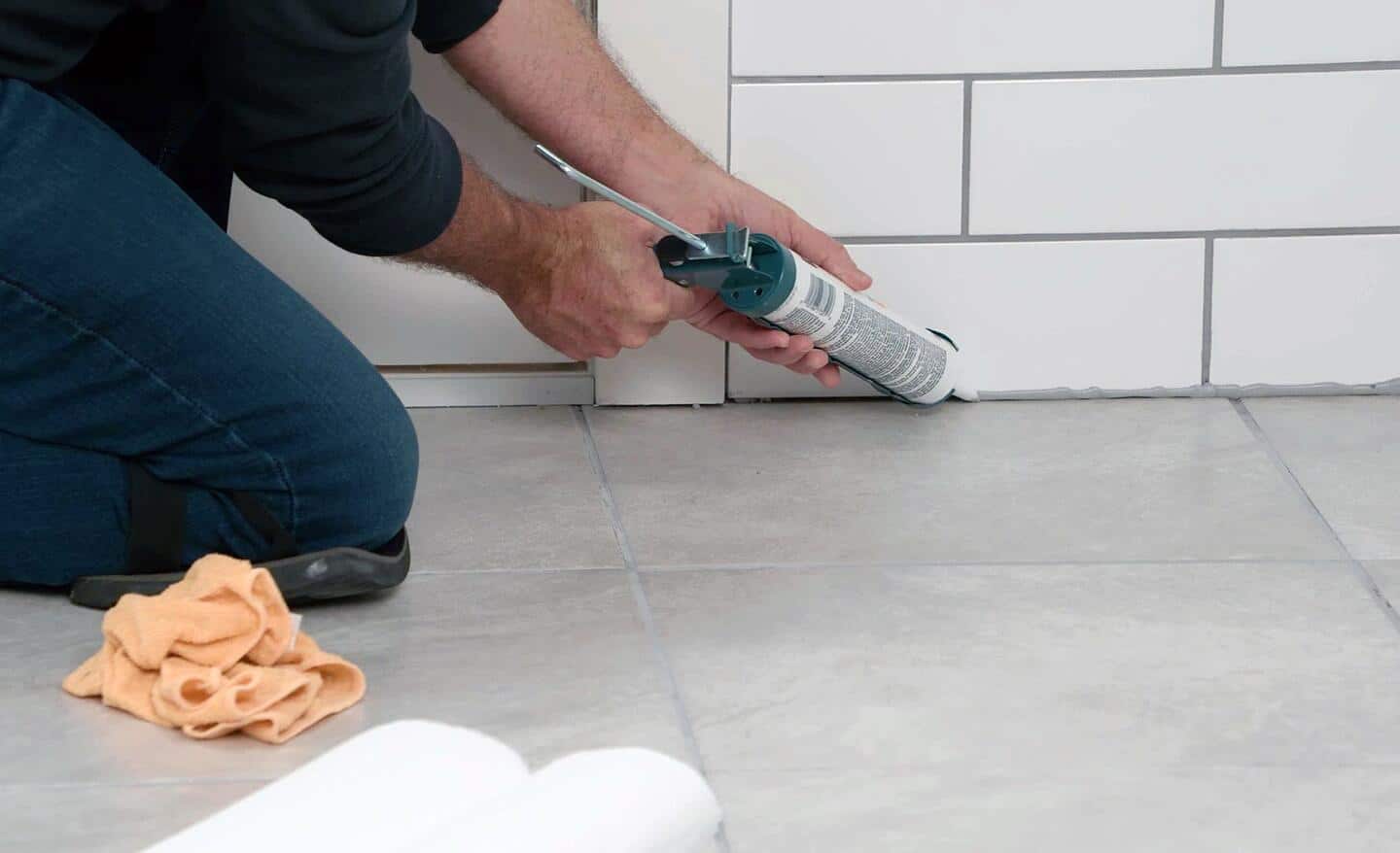 Person caulking floor tile grout at joint with wall