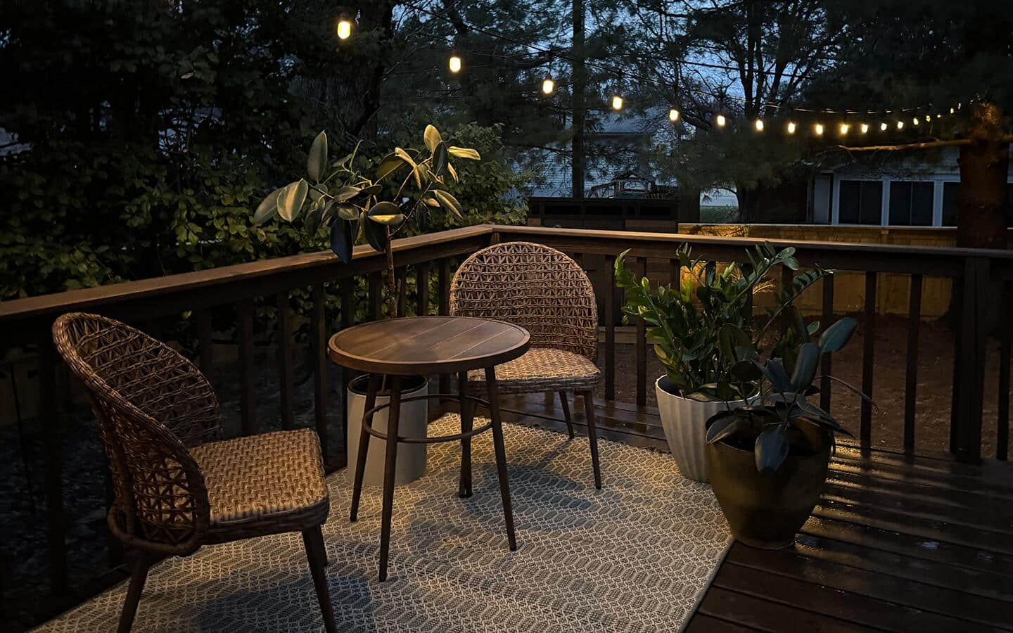 String lights illuminate a patio with two brown outdoor chairs and a matching table.