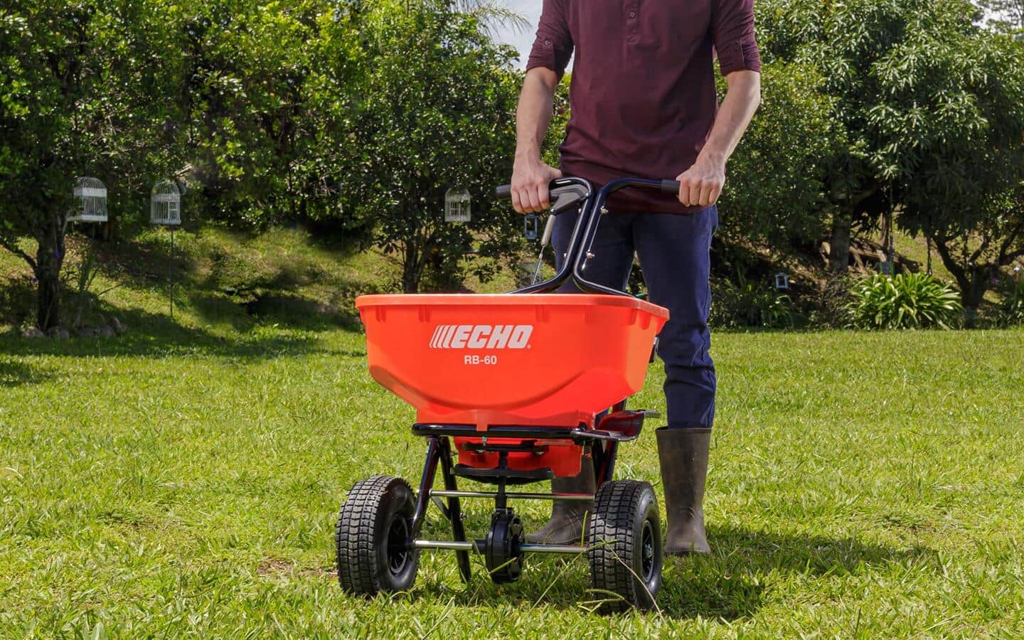 A person pushes a broadcast spreader on a lawn. A person pushes a broadcast spreader on a lawn.