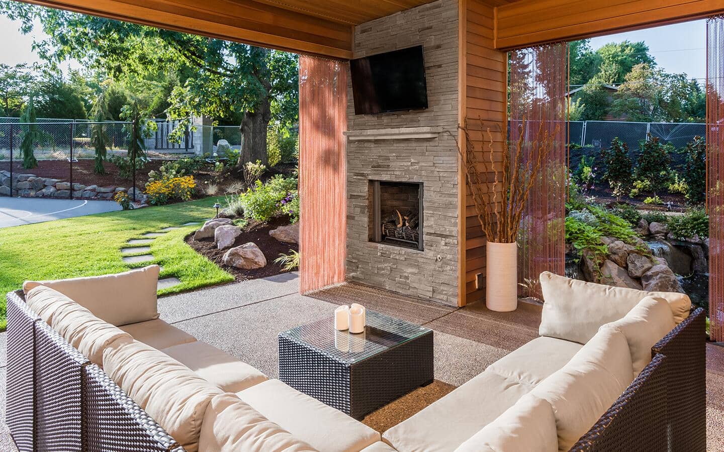 A modern, gas-fueled outdoor fireplace on a patio behind sectional seating.