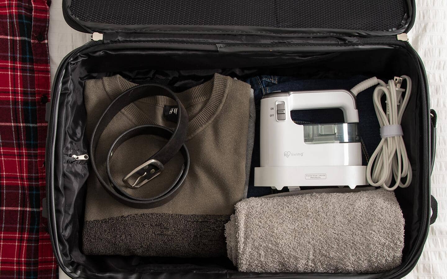 A travel iron in a suitcase with a shirt, belt and towel. A travel iron in a suitcase with a shirt, belt and towel.