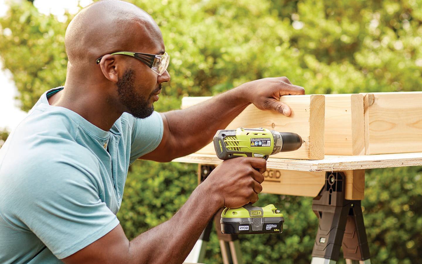 A man drills a hole in one of the boards that forms the outside of a cold frame base.
