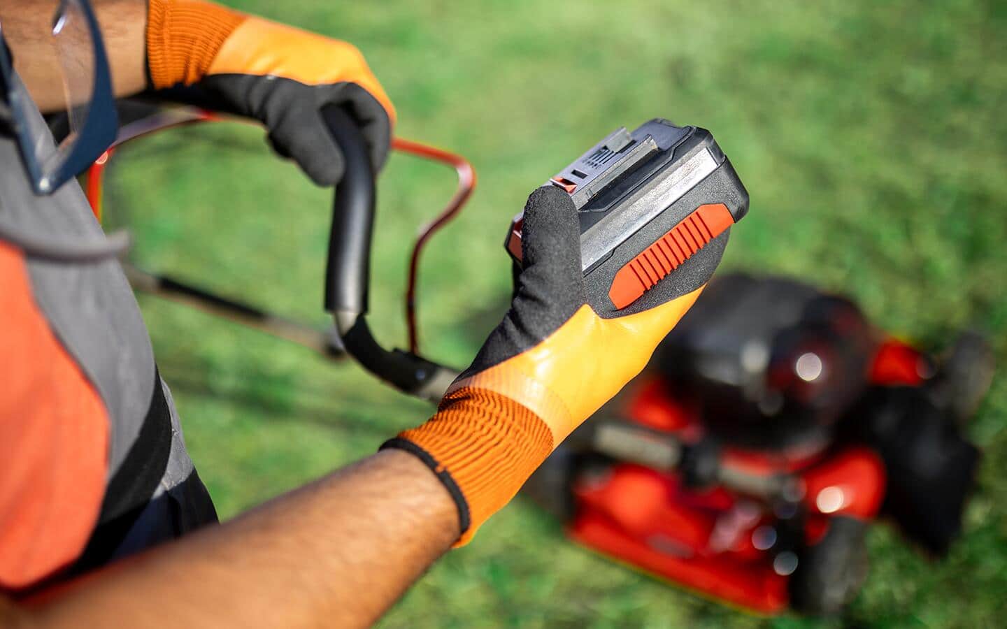 A battery is being held above a lawn mower.