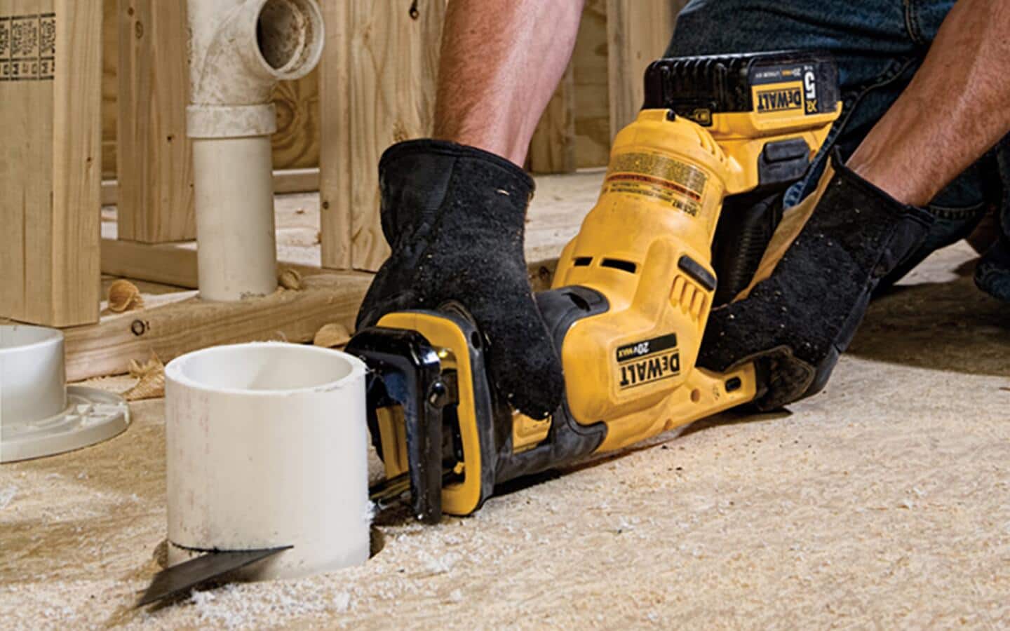 A gloved individual using a cordless reciprocating saw on a white pipe.