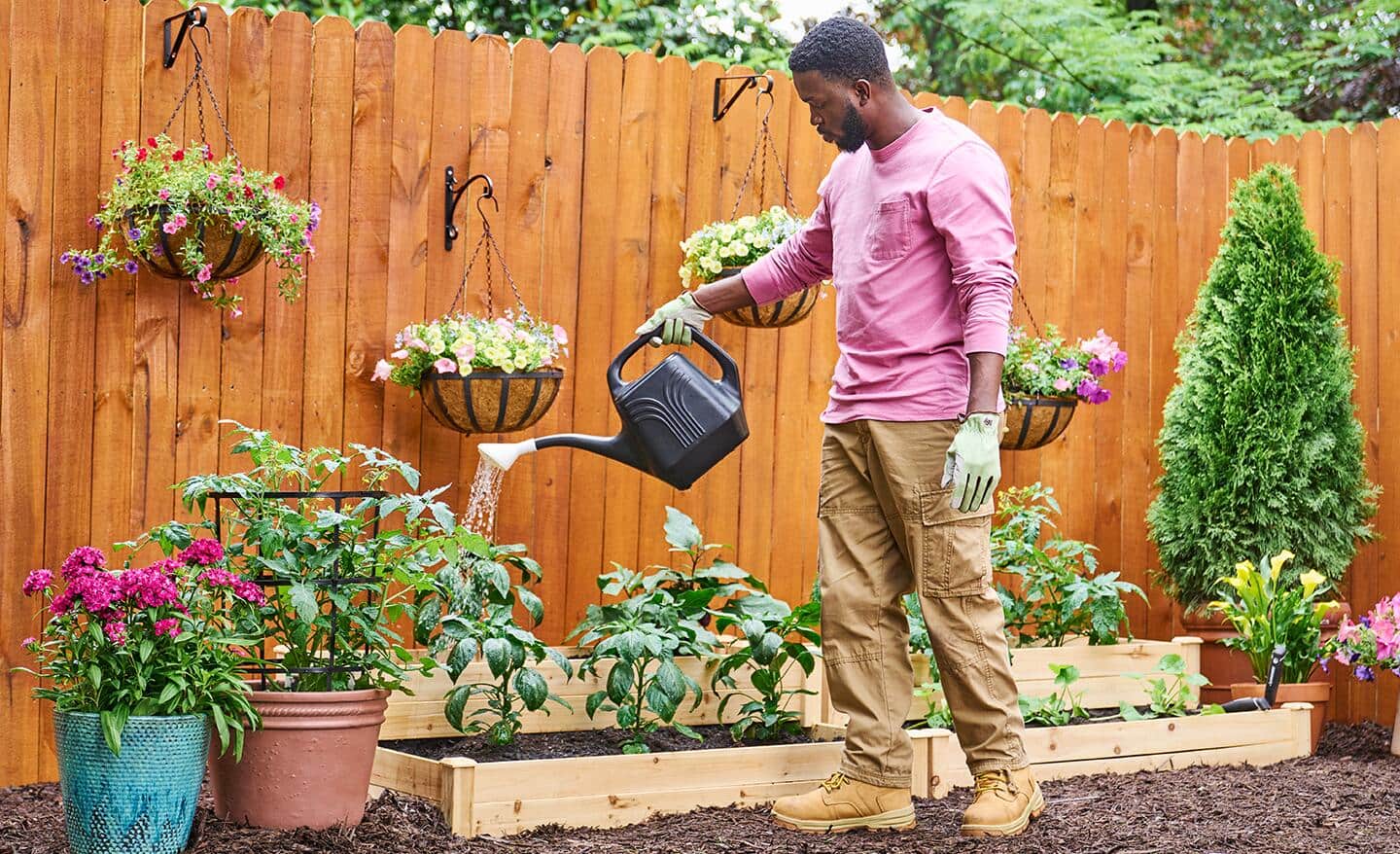 A gardener waters plants outdoors with a plastic watering can