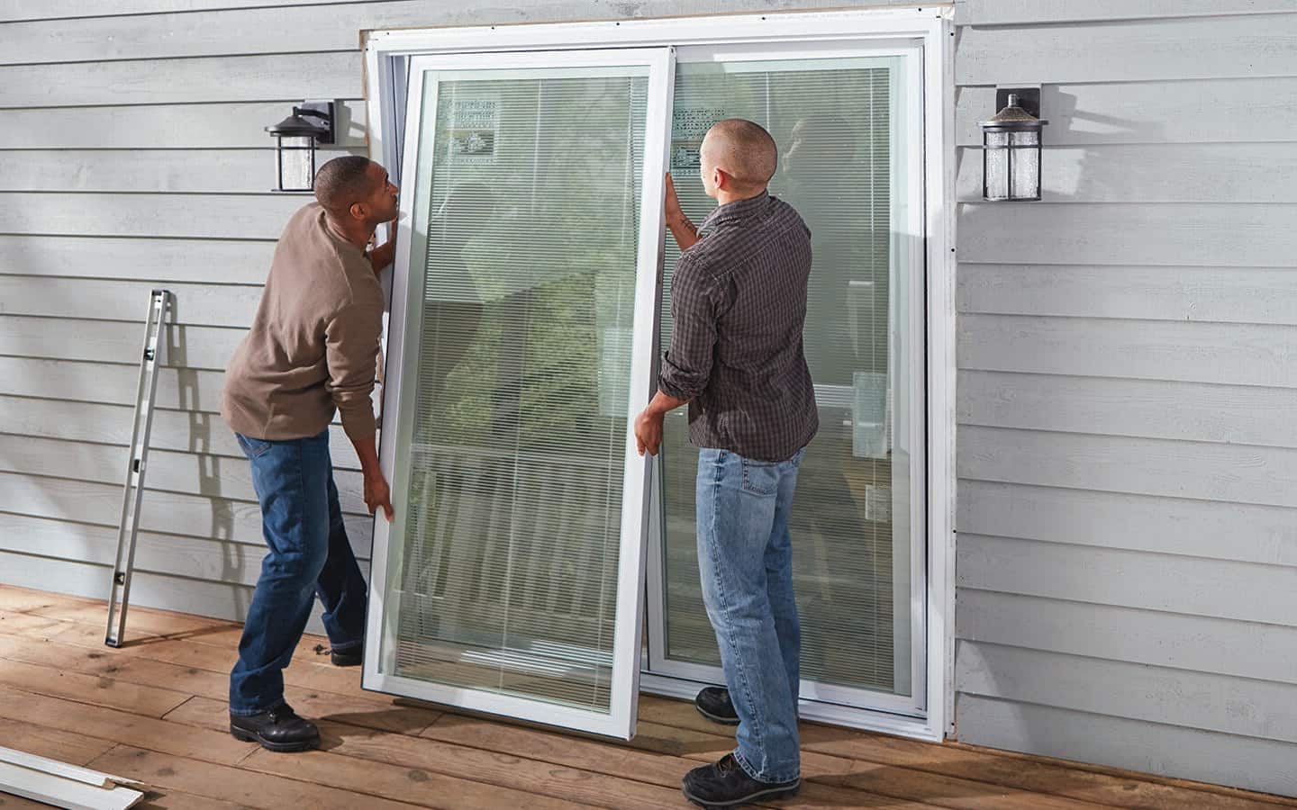 Two people stand on a deck to position a new sliding door in a frame opening.