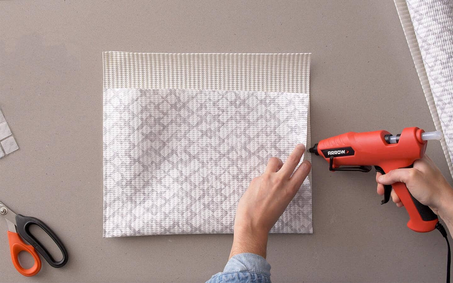 A person uses a hot glue gun to fold and seal shelf liner to make an envelope.