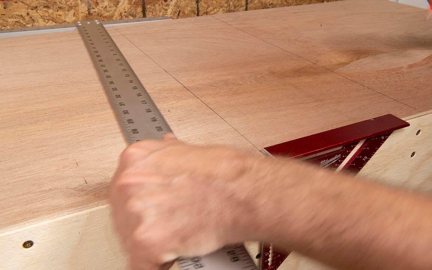 A T square and a rafter square are used to mark a line on a piece of plywood. 