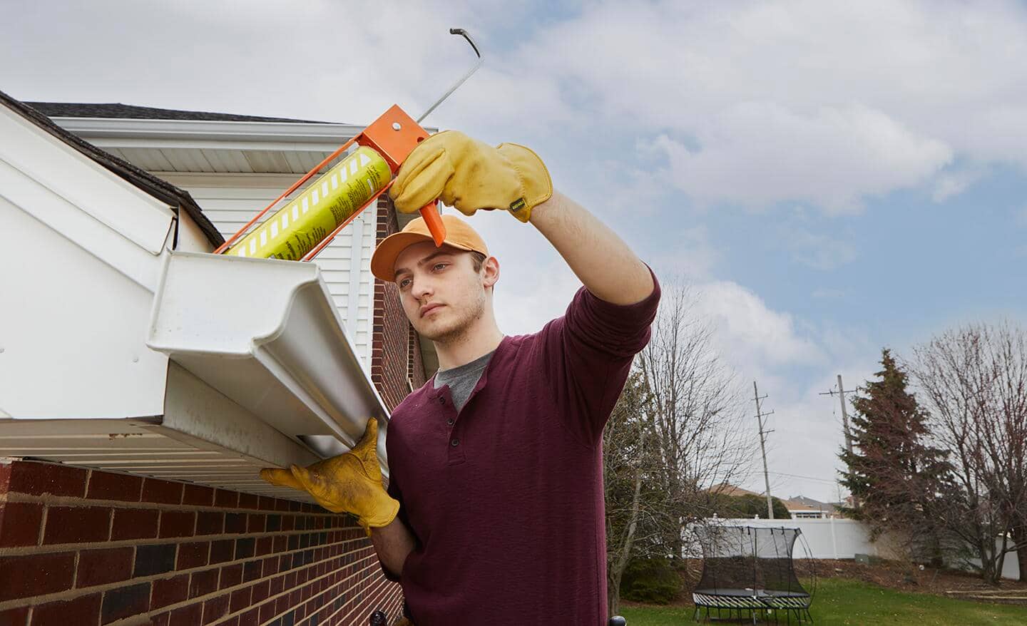 A person adding plastic roofing cement around white gutters on a roof's edge.