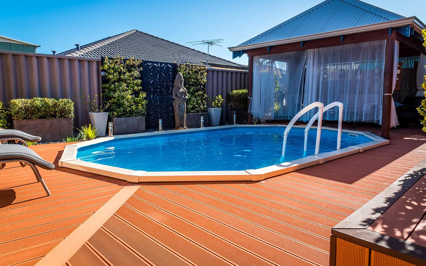A wooden deck surrounding a swimming pool in the backyard of a brick home. A wooden deck surrounding a swimming pool in the backyard of a brick home.