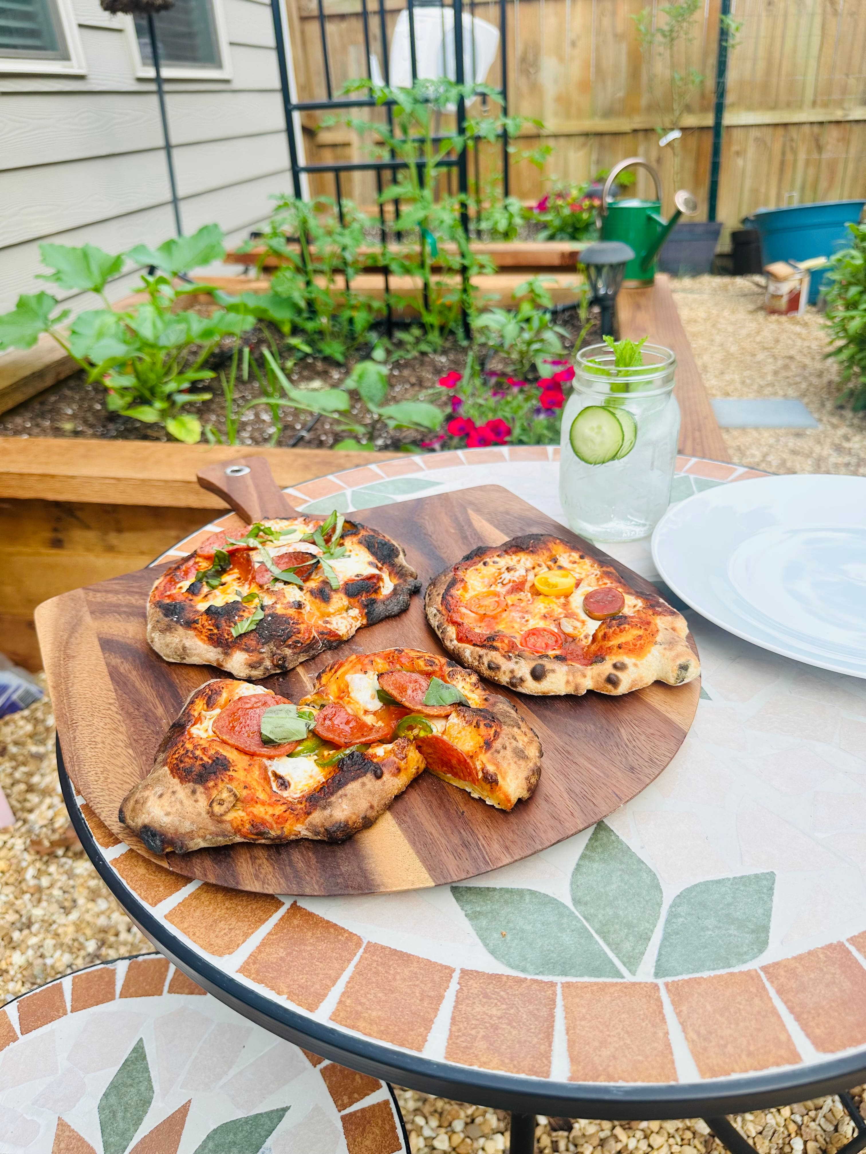 Homemade pizzas and fresh beverages sitting over a bistro table nestled in a newly revamped garden space. Homemade pizzas and fresh beverages sitting over a bistro table nestled in a newly revamped garden space.