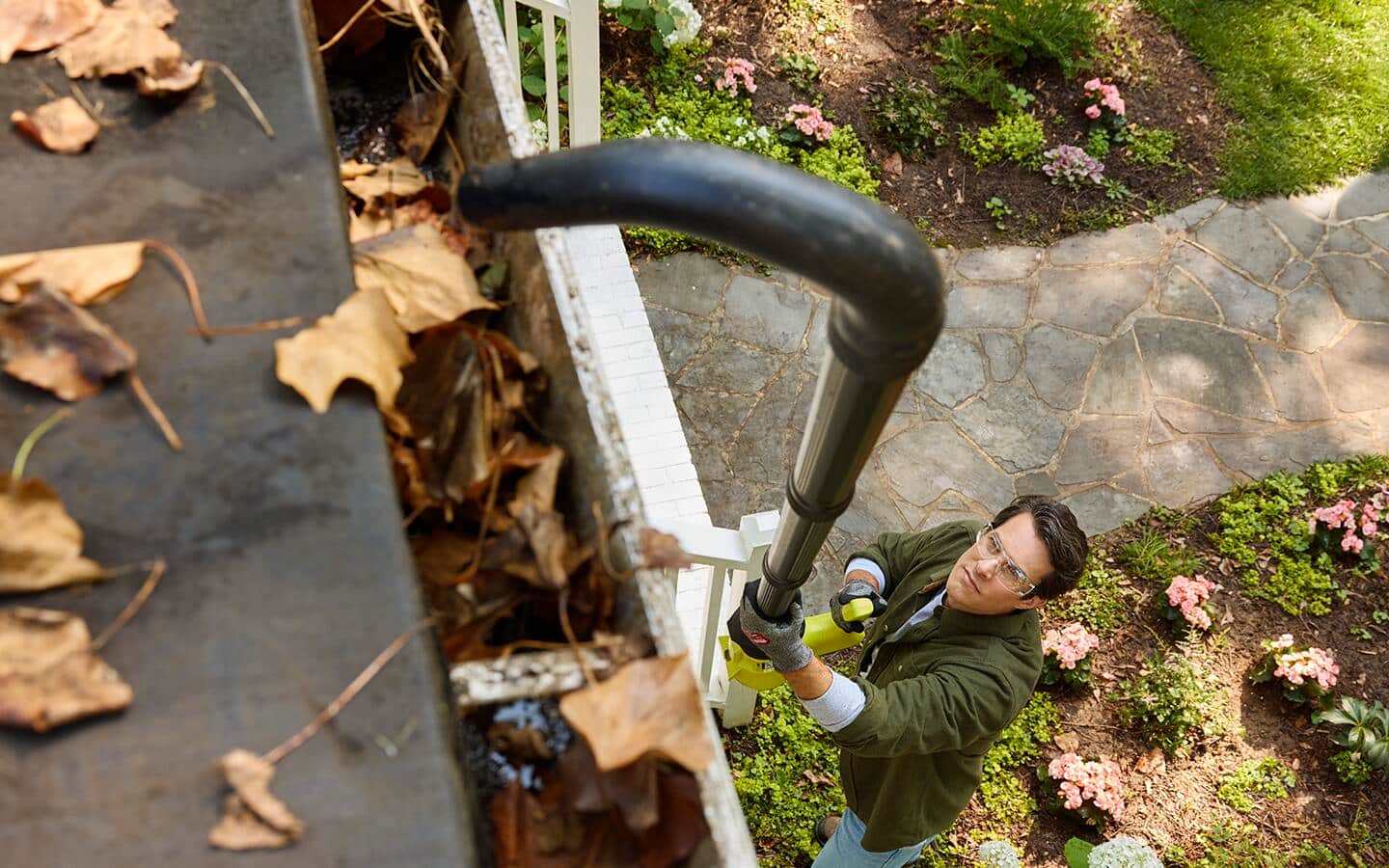 Using a gutter cleaner to remove leaves from a roof gutter.
