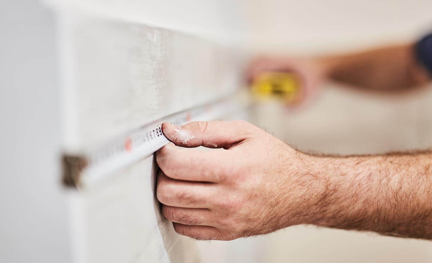 A person measuring a shower wall.