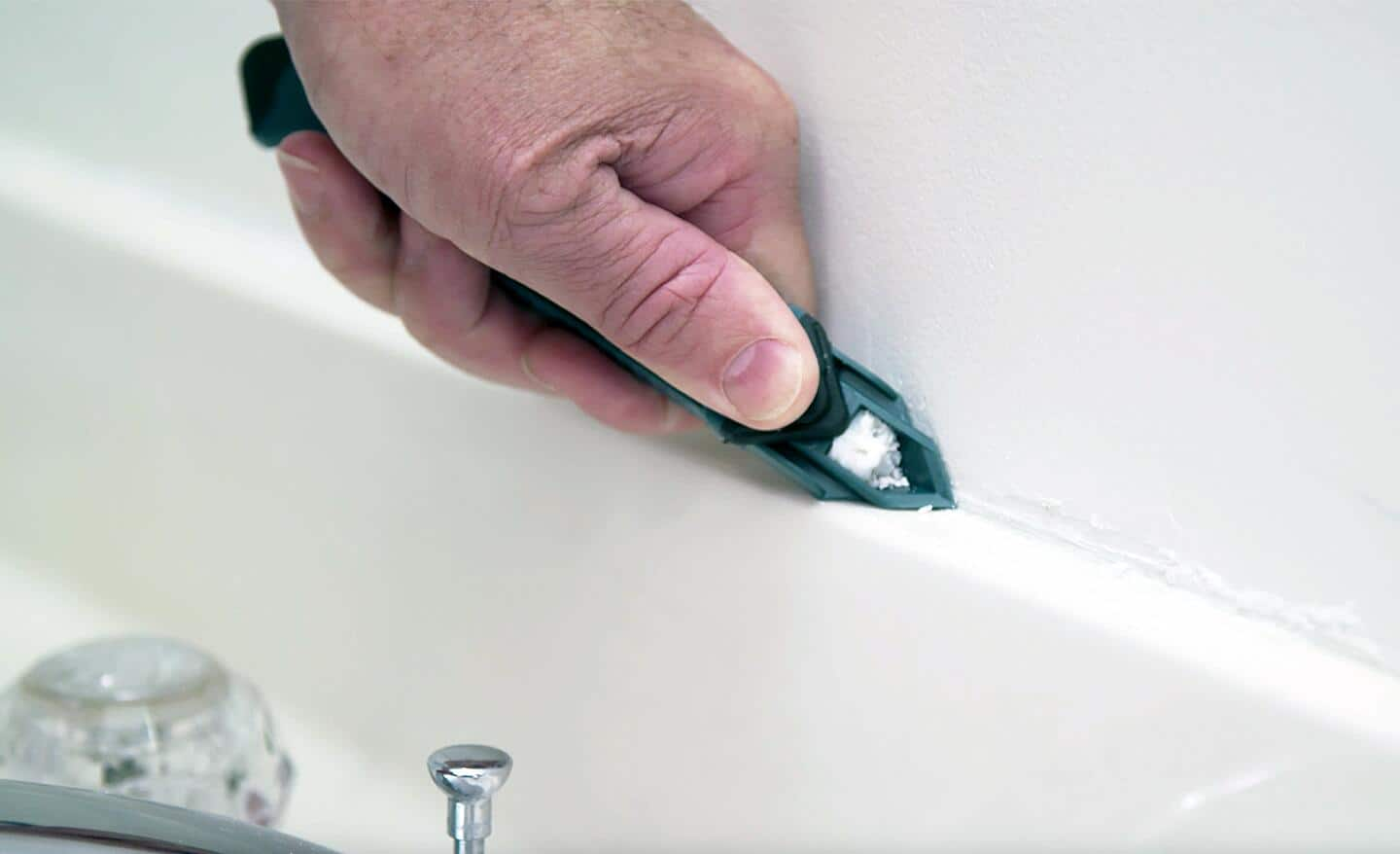 A person uses a caulk tool to remove old caulk.