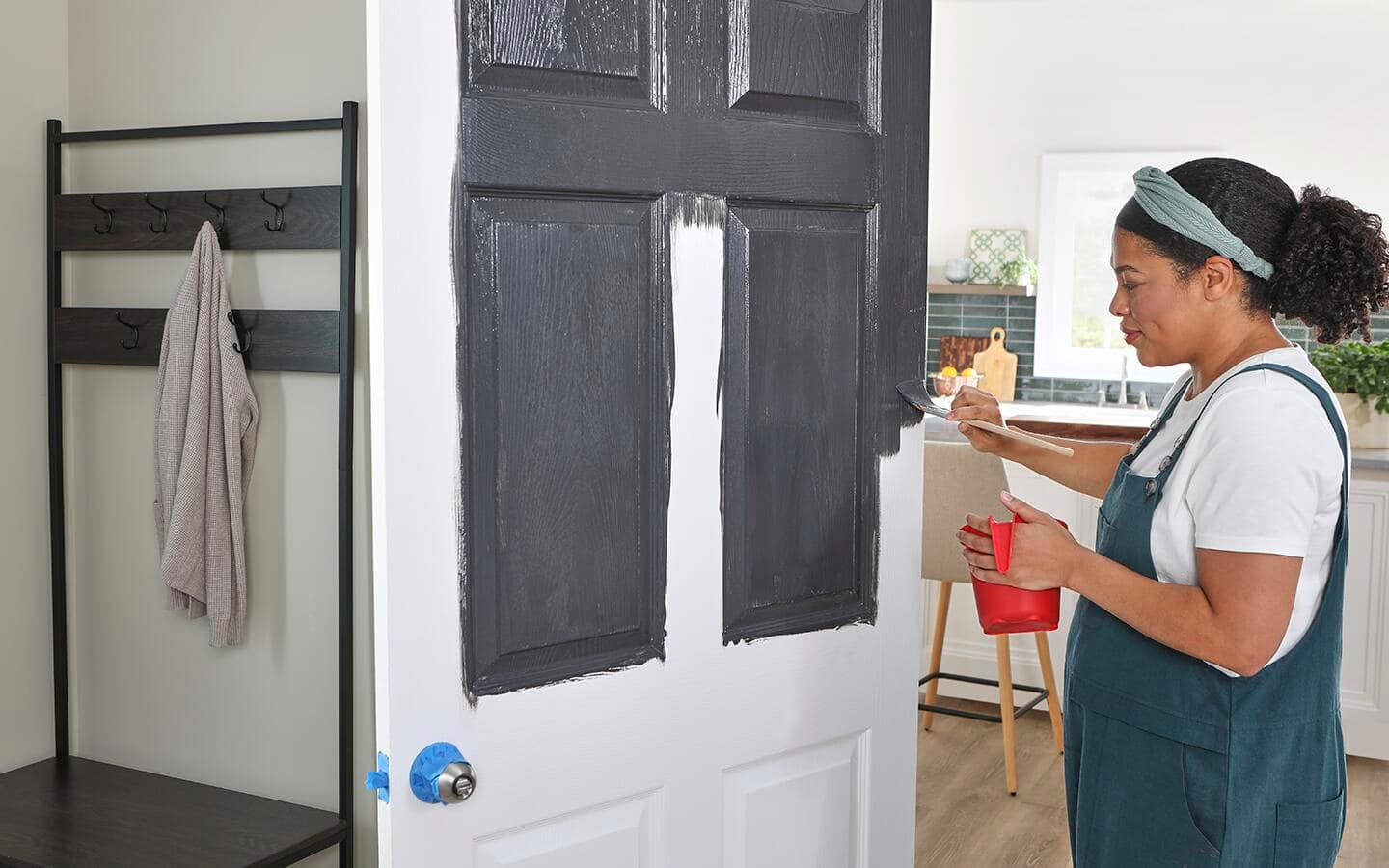 A woman paints a panel door that is still attached to the hinges. A woman paints a panel door that is still attached to the hinges.
