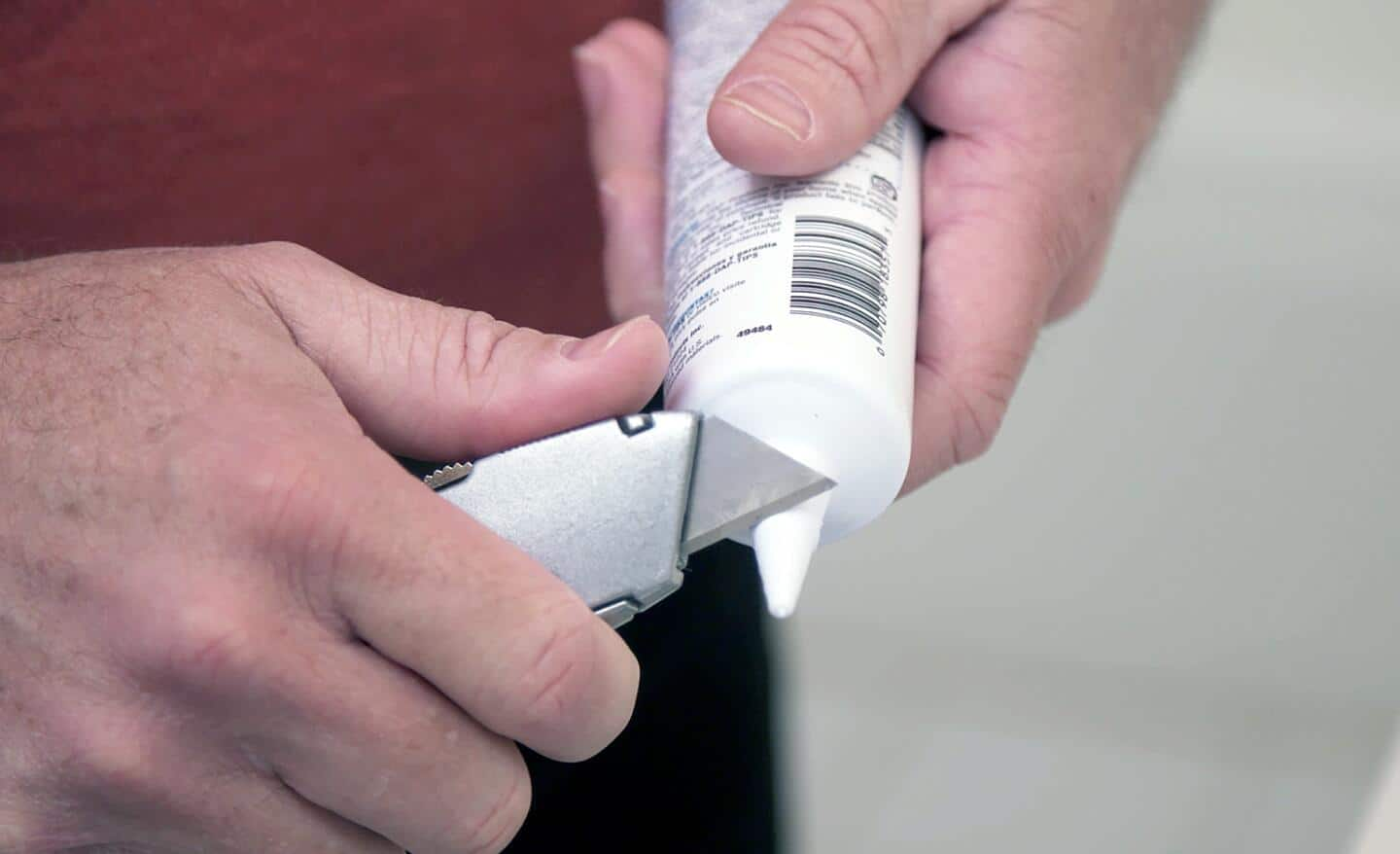 A person uses a utility knife to cut the nozzle of a caulk tube.