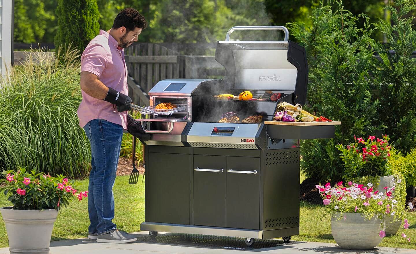 A man wearing a heat-resistant glove uses tongs to adjust food cooking on a grill.