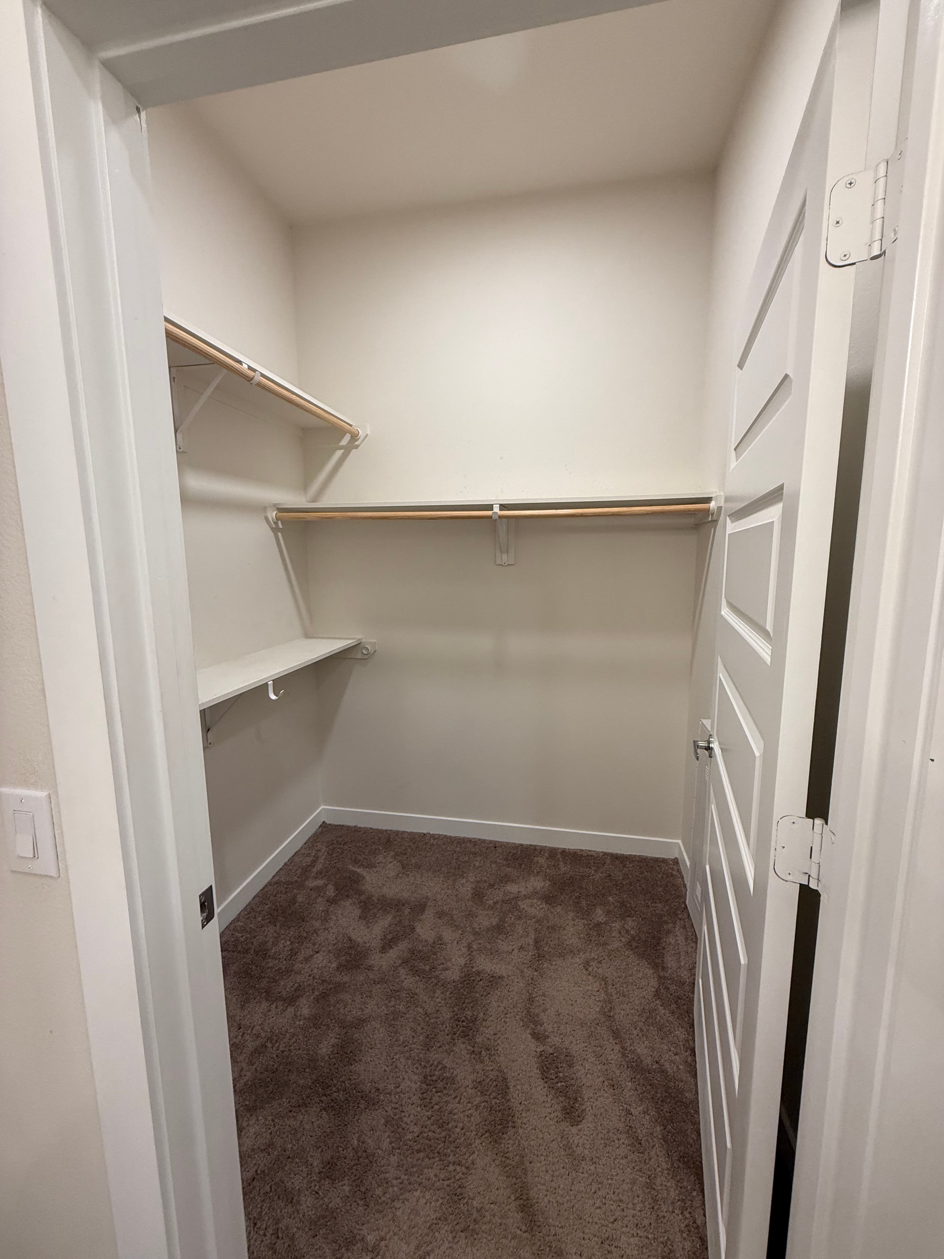 An empty walk-in closet with white walls and brown carpeting. An empty walk-in closet with white walls and brown carpeting.