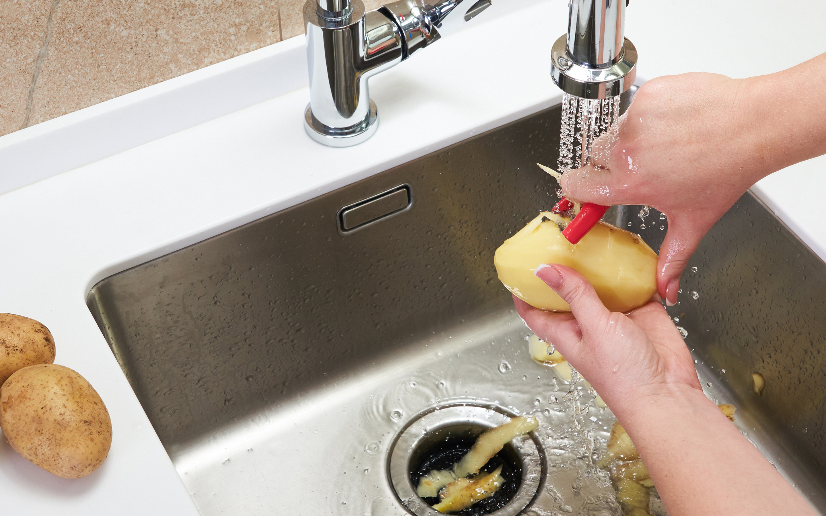 A person peeling vegetable scraps into a sink garbage disposal.