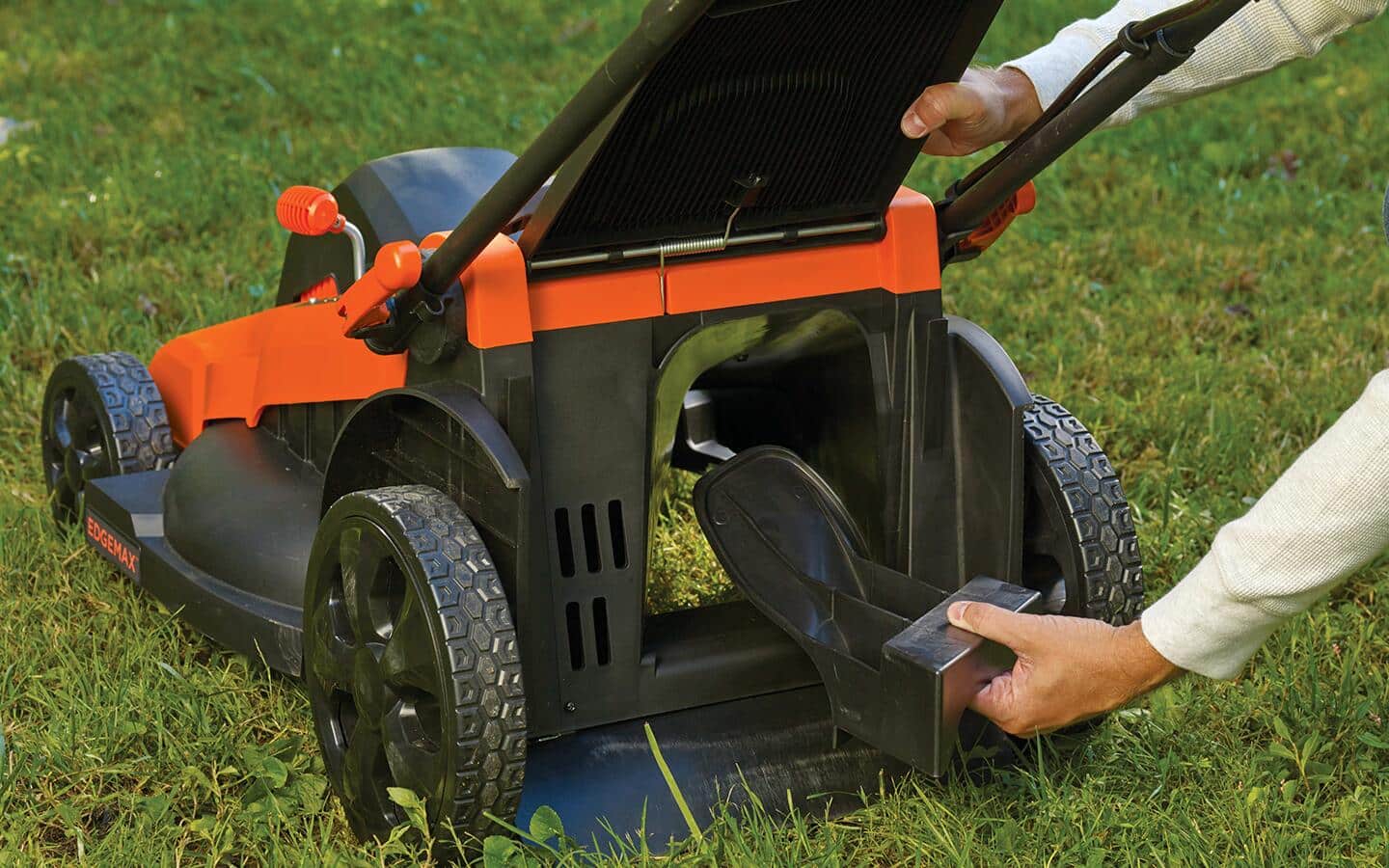 A person clears grass from a lawn mower after using it.