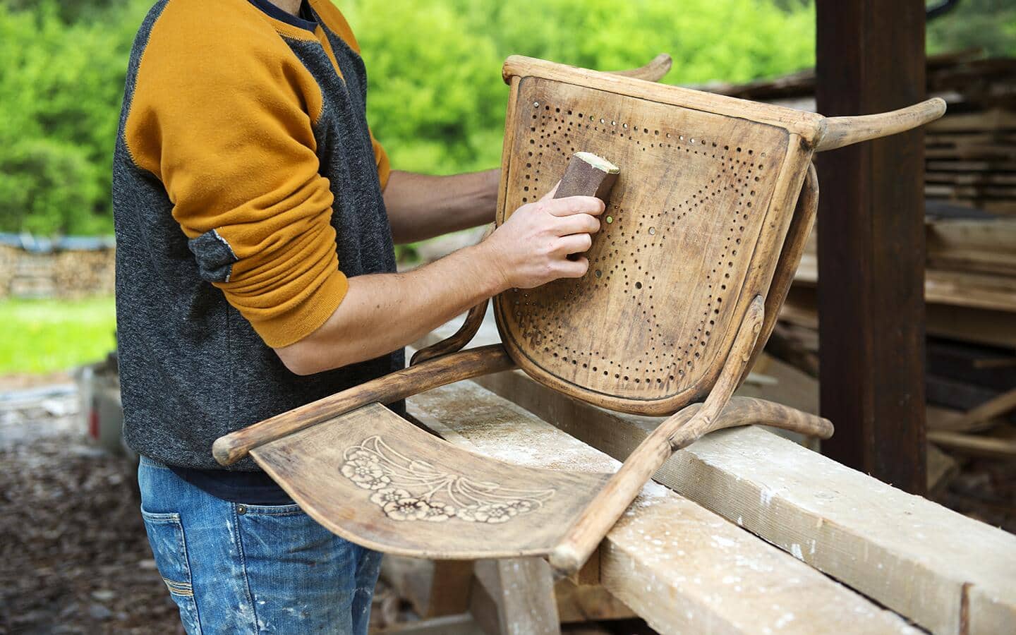 A person sands a piece of wooden furniture with a sanding block.