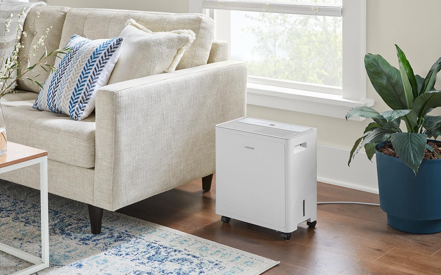 A dehumidifier sits on the floor next to a couch. A dehumidifier sits on the floor next to a couch.