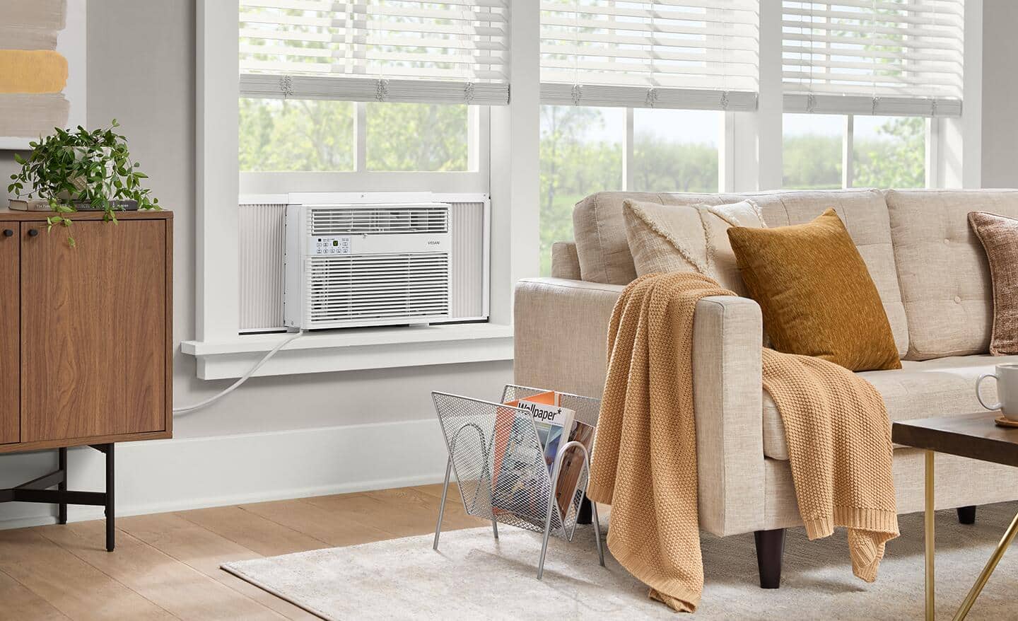 A window air conditioning unit sitting in a living room behind a beige couch.