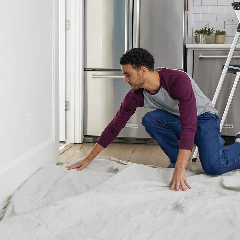 A person putting a drop cloth down on a floor.