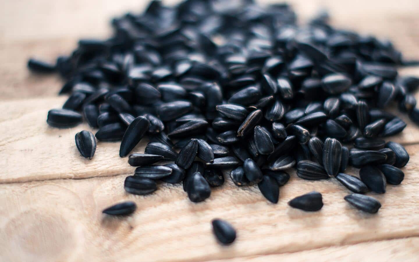 A pile of black oil sunflower seeds on wood.