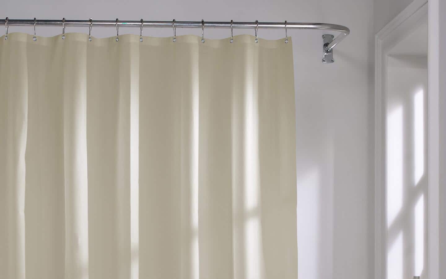A beige vinyl shower curtain hanging on a circular silver rod in a bath.