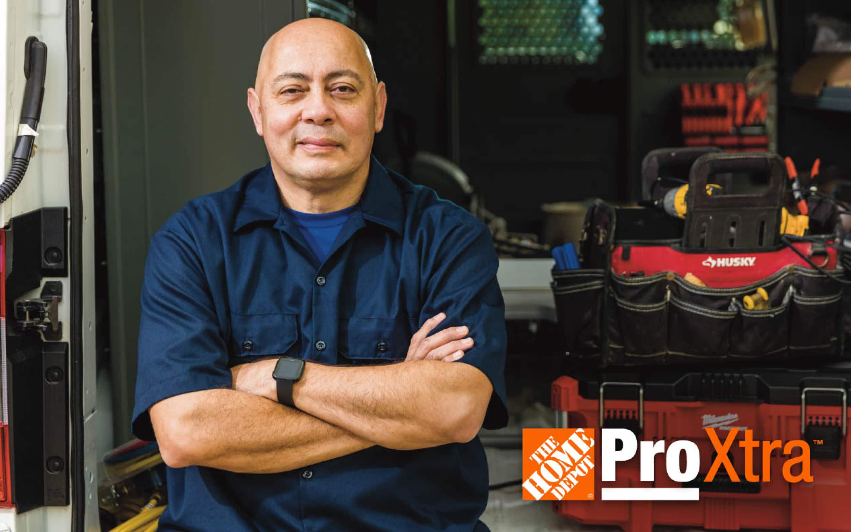 A contractor with his arms crossed, leaning against his work truck, which features tools and The Home Depot Pro Xtra logo.