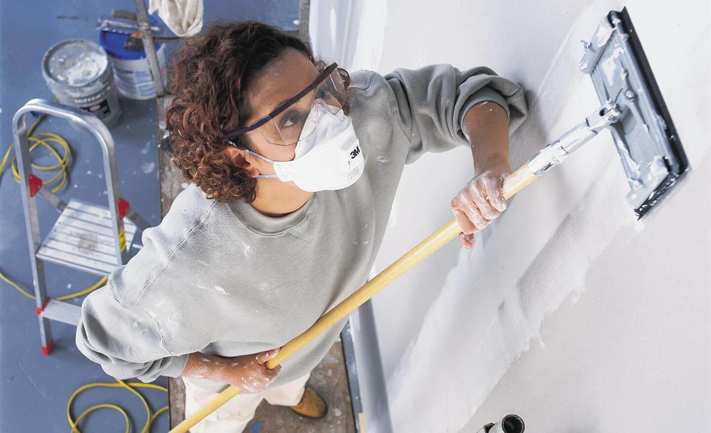 A woman uses drywall screen on an extension handle.