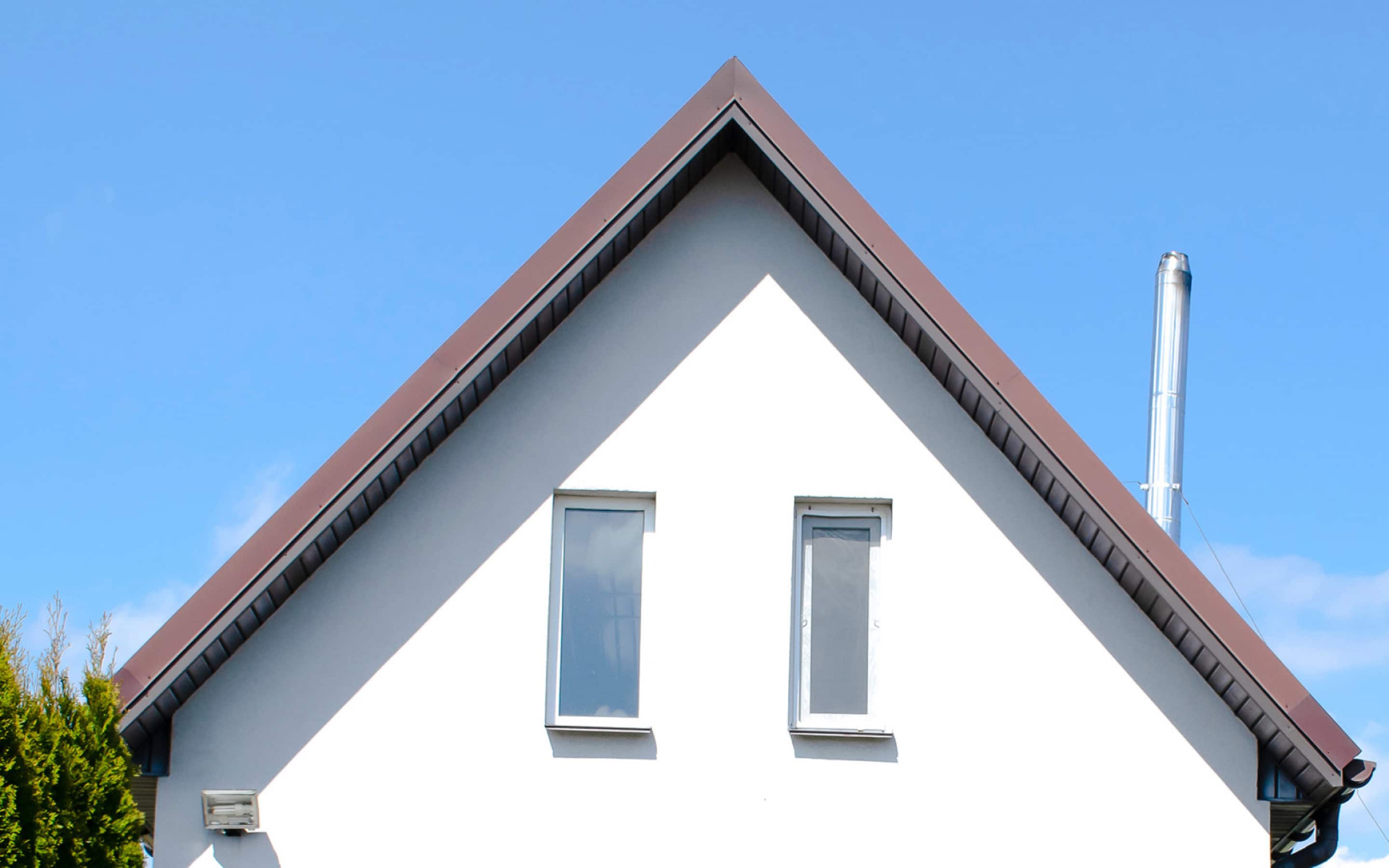 The gable of a house with a brown gabled roof, two windows, and a metal chimney, set against a blue sky.