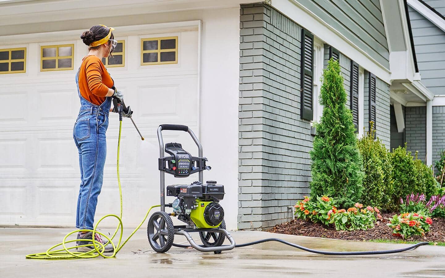 A woman cleaning a driveway with an electric pressure washer.