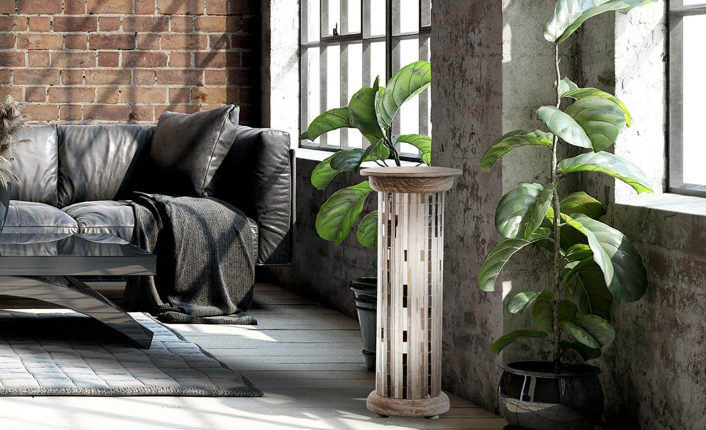 A column lamp shines brightly next a black sofa and a brick wall. 