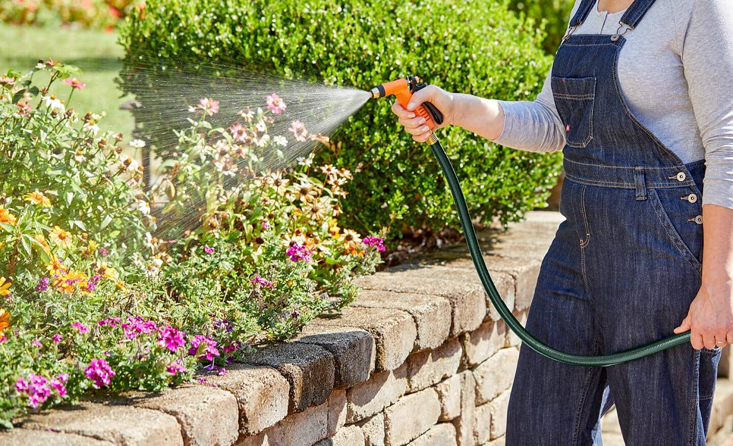 Gardener using a hose nozzle to spray a flower bed