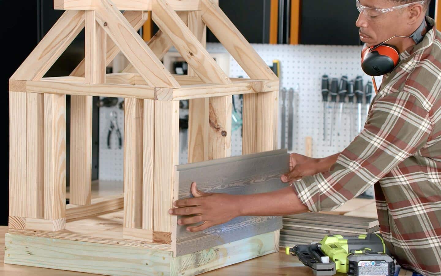 A person places cedar boards for siding on a dog house.