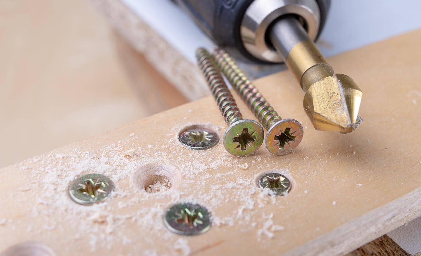 A drill and screws on a piece of wood.