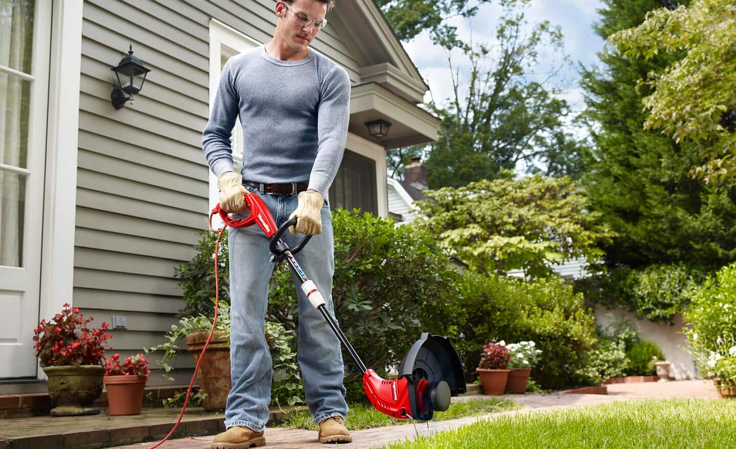 A person uses a gas string trimmer to edge flower beds.